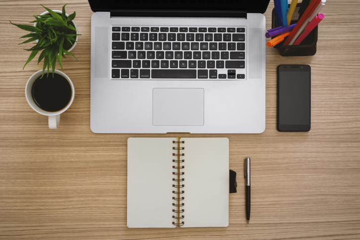 A laptop on a desk next to a notebook and a cup of coffee, creating the perfect work life setup.